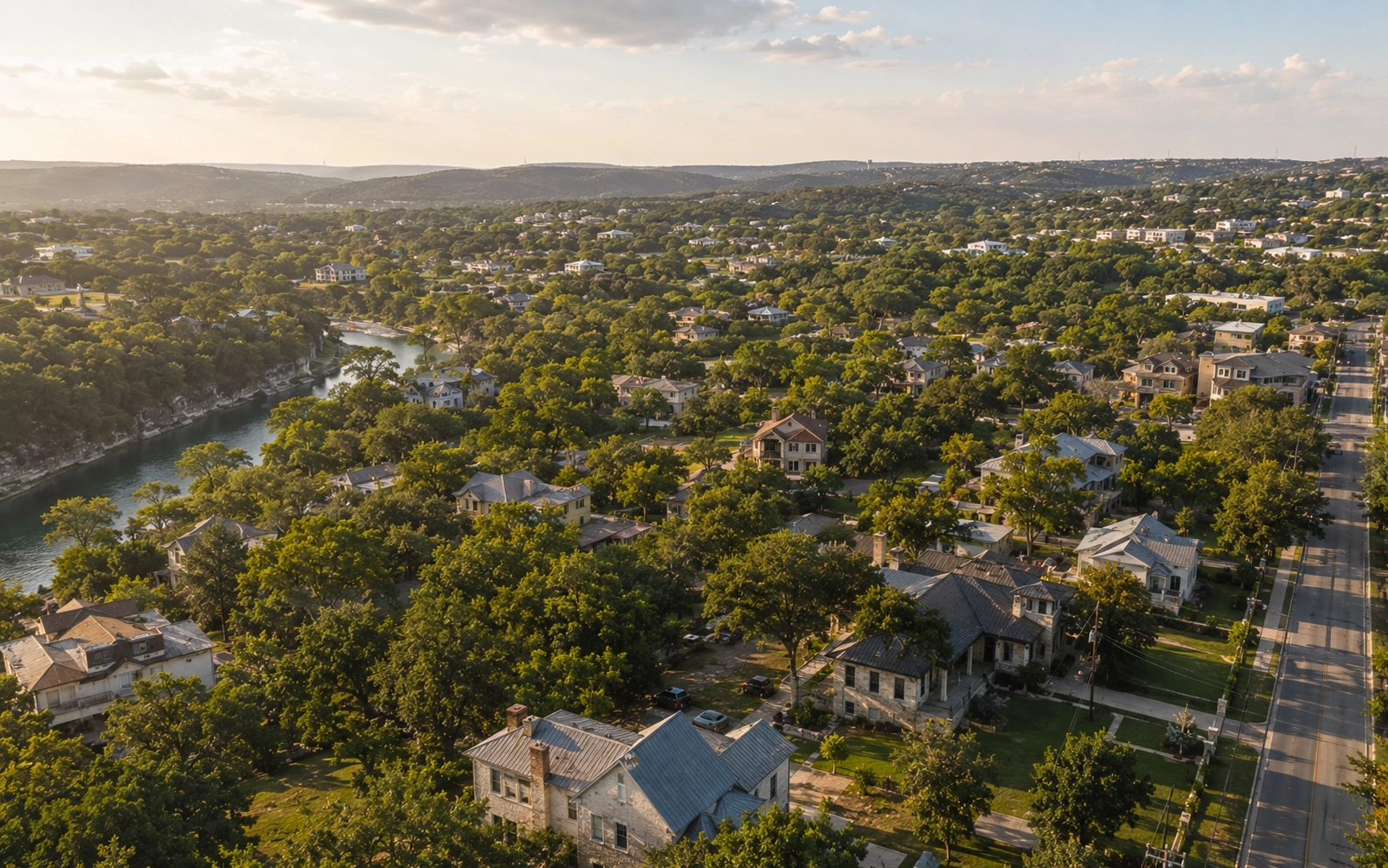 Aerial editorial photograph of a Hill Country residential neighborhood near New Braunfels with rolling oak canopy and soft late afternoon light.