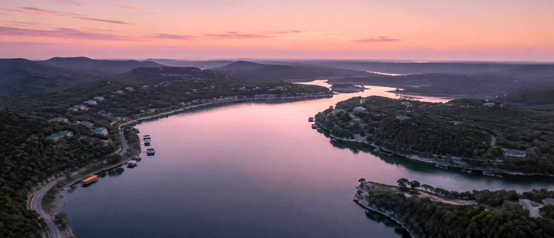 Aerial dawn photograph of Canyon Lake with folded Hill Country ridges and soft pink water.