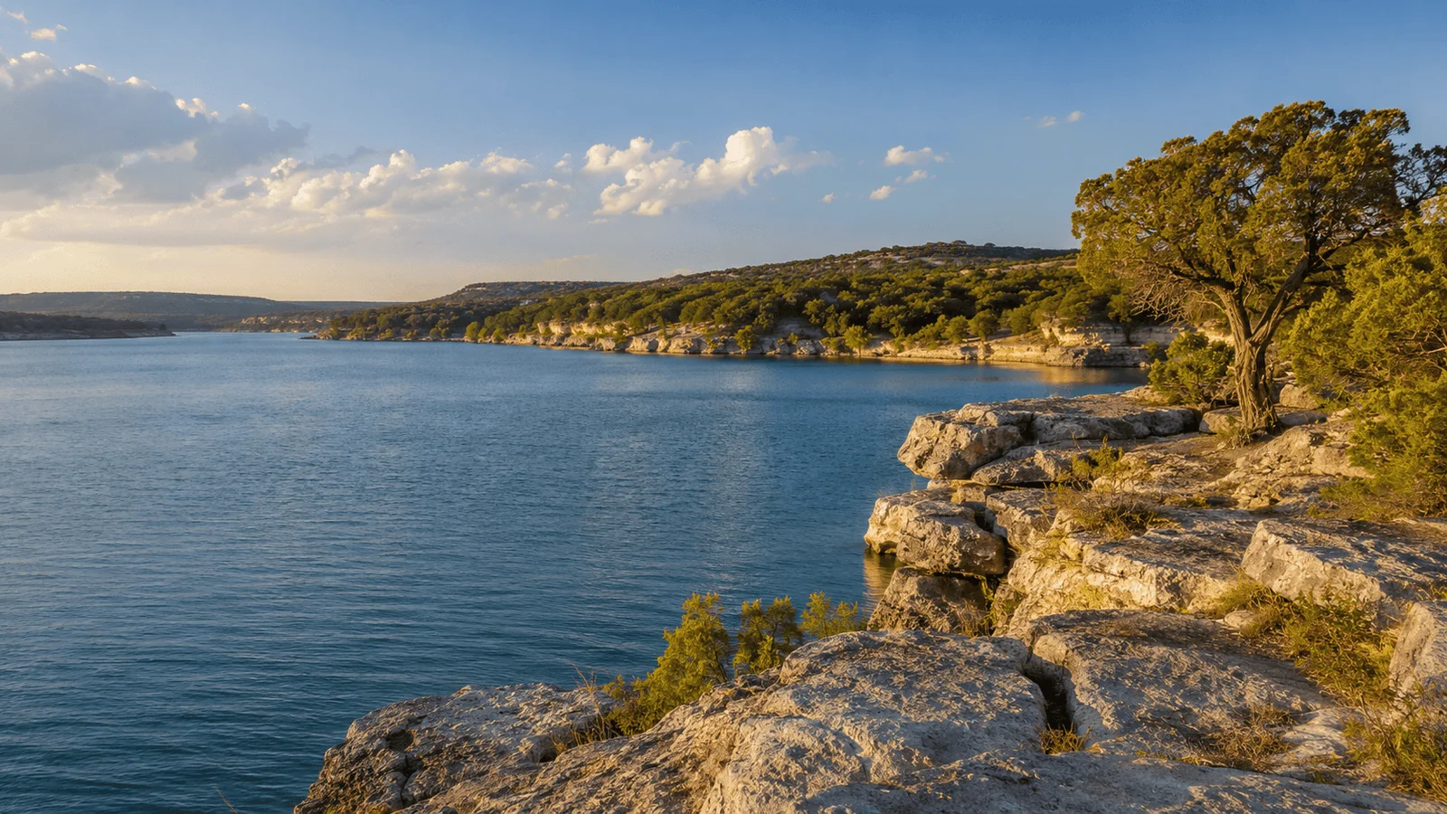 Aerial view of Canyon Lake shoreline with Hill Country homes nestled among cedar trees reflecting on clear blue water at golden hour