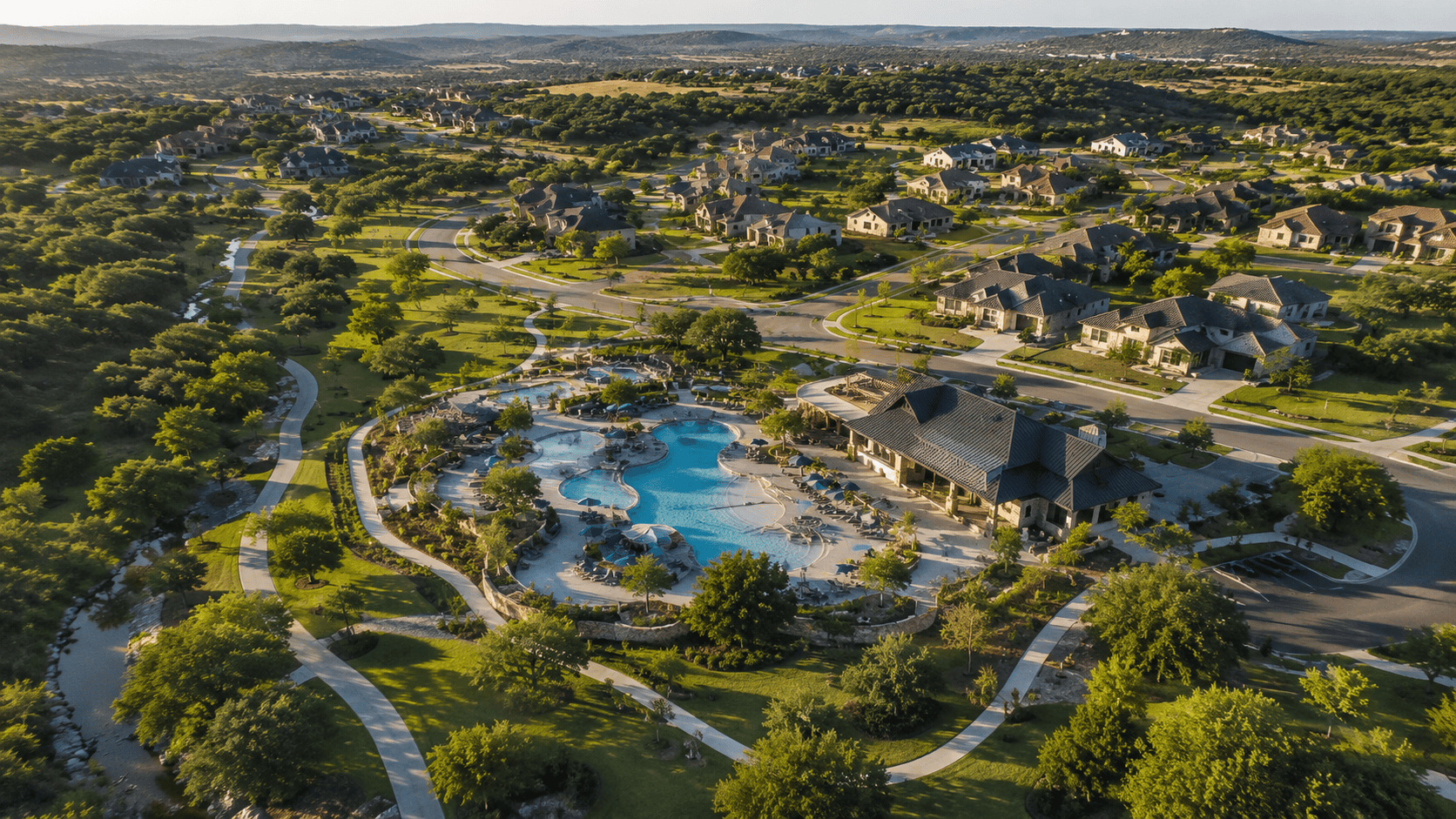 Aerial view of Veramendi master-planned community in New Braunfels, Texas, showing tree-lined streets, resort-style pool, and Hill Country landscape at golden hour