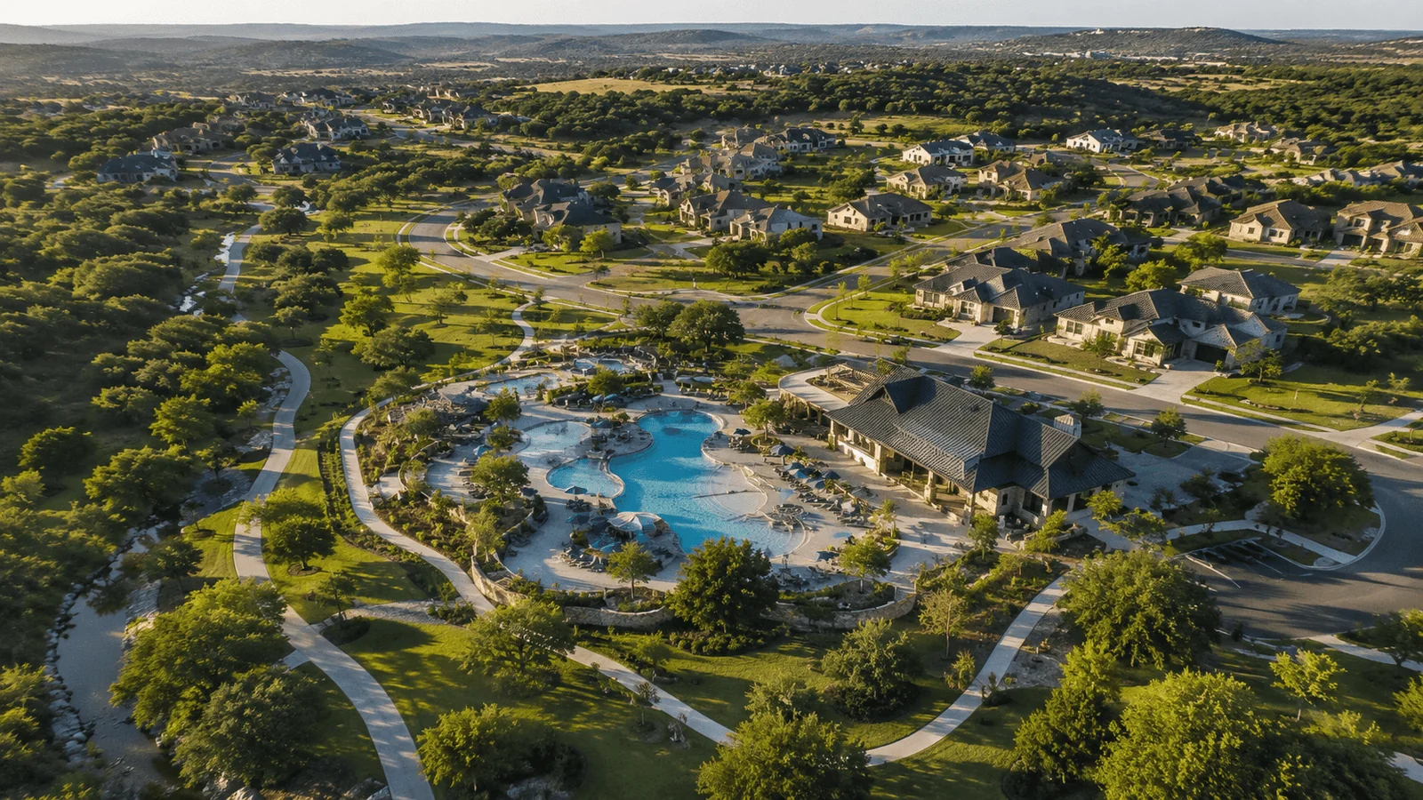Aerial view of Veramendi master-planned community in New Braunfels, Texas, showing tree-lined streets, resort-style pool, and Hill Country landscape at golden hour