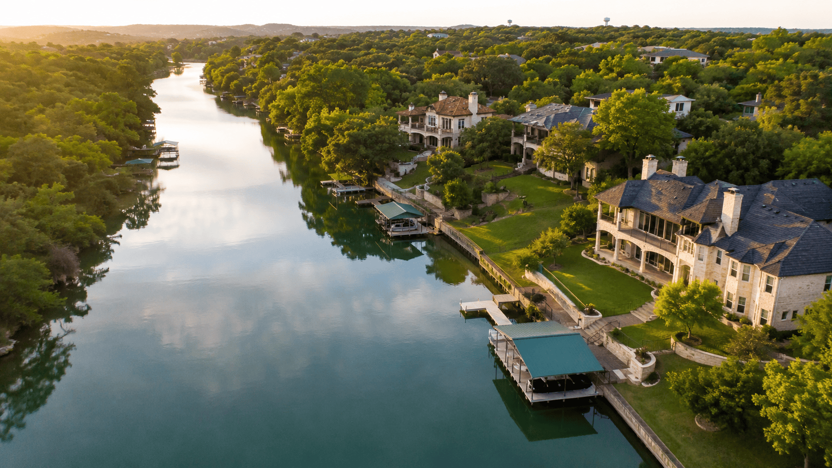 A cypress-lined river with a limestone home nestled along the bank in the Texas Hill Country, afternoon light filtering through the trees